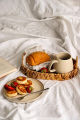 Cozy breakfast with coffee, croissant and fresh strawberries on a wicker tray in natural morning light. Minimalistic home lifestyle concept.