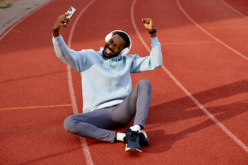 Triumphant male athlete celebrates success by cheering and raising his fists while sitting on a...