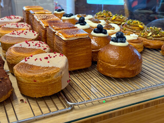 Fresh pastries and brioche buns with cream and blueberries in bakery display. Modern European pastry trends