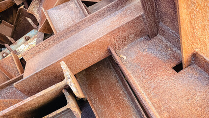 Close-up of a chaotic pile of heavily rusted metal I-beams, creating an industrial abstract...