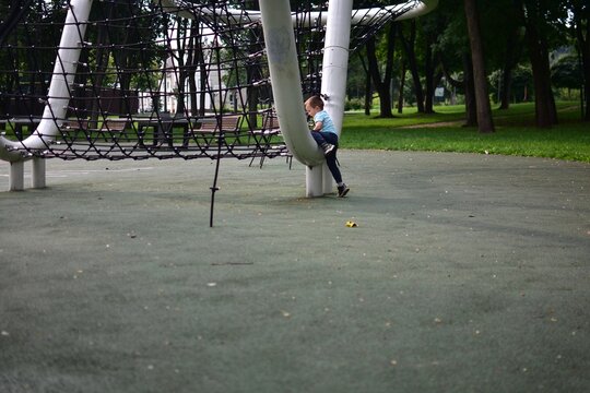 Boy climbing up large curved metal playground tube with net structure outdoors, focused effort and determination, green park environment, physical development and adventure.