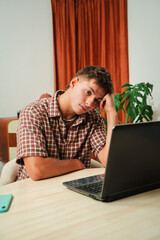A young man displays visible frustration while working on a laptop, showing signs of stress and confusion as he contemplates a problem that is clearly bothering him. He appears deep in thought.
