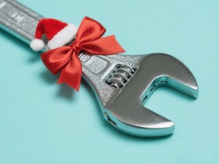 A shiny metallic wrench decorated with a Santa hat and red bow for Christmas. Festive holiday tool concept for a handyman or repair service promotion