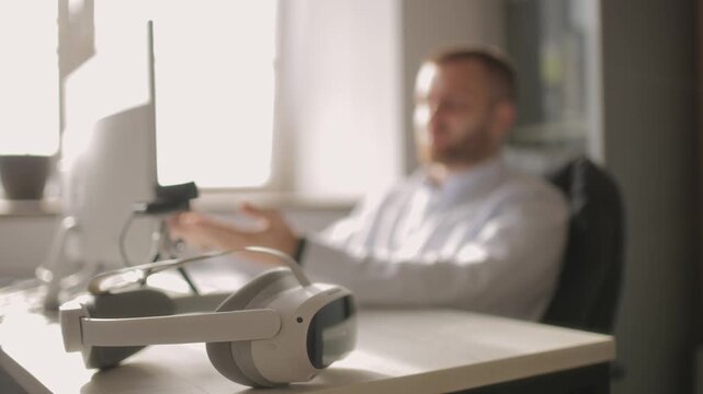 Closeup virtual reality headset in modern office setting on background man working on computer in call on video meeting. - Powered by Adobe