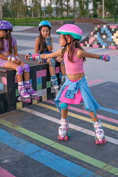 A girl and her friends are roller skating in a skatepark. Children learn to keep their balance by roller skating