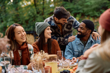 Cheerful friends gathering for meal at picnic table in backyard in autumn.