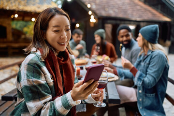 Happy Korean woman using smart phone while having lunch with friends in backyard in autumn.