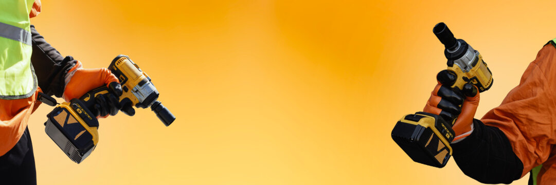 Two construction workers holding cordless drills on a bright yellow background. Concept for teamwork, modern construction tools, efficiency and industrial power. - Powered by Adobe