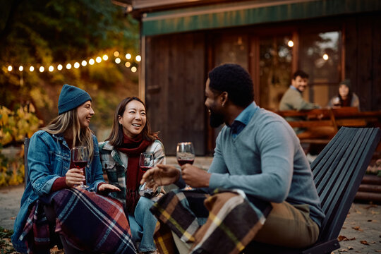 Happy friends drinking wine and communicating while enjoying in autumn day on patio.