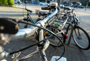 Parked bicycles in a sunlit urban setting, highlighting chrome handlebars, black grips, and communal bike infrastructure in the afternoon light.