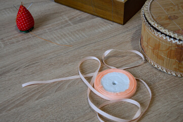 peach ribbon roll on wooden table with sewing accessories, strawberry pincushion and craft box, concept of handmade work, tailoring, DIY crafts, gift wrapping, and creative design materials