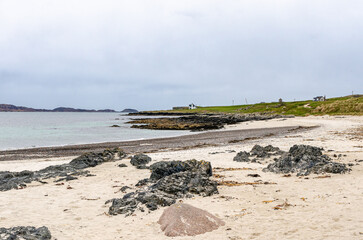 Quiet beach with rocks and soft sand along Iona near the Isle of Mull coastline, Scotland. Peaceful seascape under cloudy sky.