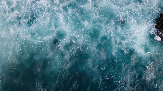 Turbulent ocean water around volcanic reefs and boulders, top down view