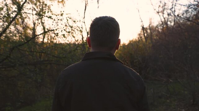 A man walks forward through a forest at sunset, seen from behind. The warm evening light creates a peaceful and cinematic atmosphere as he moves into the golden horizon.