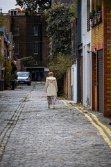 eine Dame mit Hut geht eine enge Gasse in London entlang