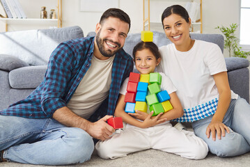 Happy family playing colorful blocks together, fun time at home. Cheerful parents and daughter sit...