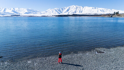 Person standing on a lakeshore of Tekapo with stunning snow-covered mountains. New Zealand
