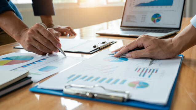 Business team collaborating over charts and reports, reviewing financial data on paper and laptop, discussing strategy, planning and analysis during a professional office meeting