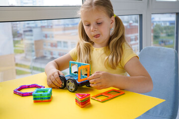 The photo shows a little girl creatively playing with magnetic building blocks, constructing...