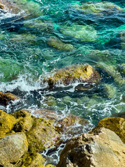 Vibrant ocean waves crashing against colorful rocks in a clear tropical bay during daytime