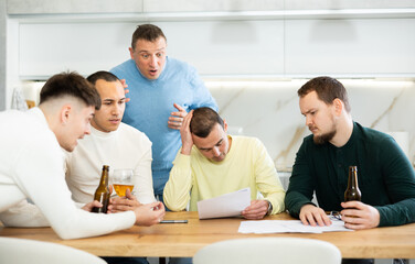 Male friends read a financial or legal document, drink beer and try to solve financial problems by consulting each other while sitting at the table