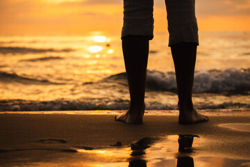 Person standing barefoot on beach during sunset