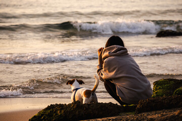 Woman with dog watching sea waves at sunrise