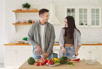 Happy smiling young couple cooking together and looking at each other in kitchen. Cheerful man and...