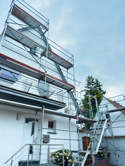 Renovation project underway on a charming white house surrounded by scaffolding under a cloudy sky in a quiet neighborhood