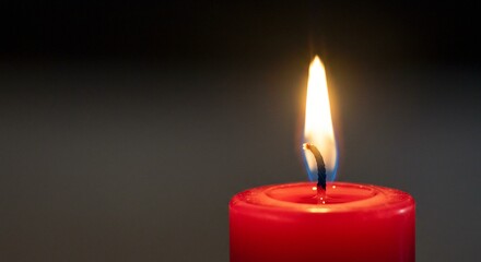 A vibrant red candle is lit, casting a warm glow in the dark, evoking feelings of peace and relaxation at night.