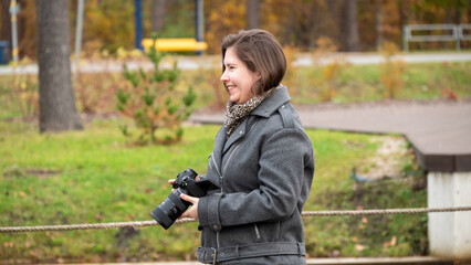 Woman Smiles While Holding Camera Outdoors in a Park During Autumn Season