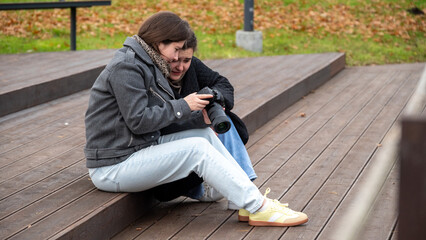Two Friends Sharing a Moment While Reviewing Photos on a Camera Outdoors in a Park During Autumn