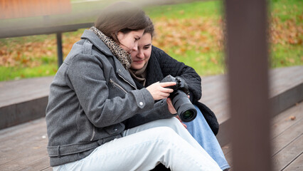 Two Friends Sharing a Moment While Looking at Camera Pictures on a Fall Day in the Park