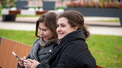 Two Friends Relax on a Park Bench Enjoying Their Time Outdoors While Using Their Phones in a Vibrant Setting