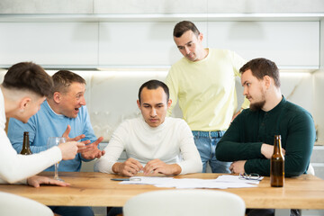 Male friends read a financial or legal document, drink beer and try to solve financial problems by consulting each other while sitting at the table