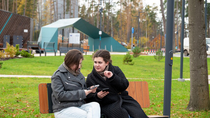 Friends Chatting and Sharing Information on a Smartphone in a Park During Autumn in a Modern Urban Area