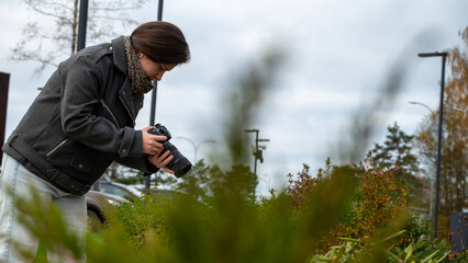 Woman Captures Nature's Beauty With Camera in Urban Garden During a Cloudy Afternoon