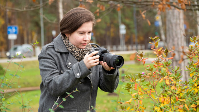 Young Woman Captures Nature With Camera While Enjoying a Peaceful Autumn Day in a Park Surrounded by Colorful Leaves