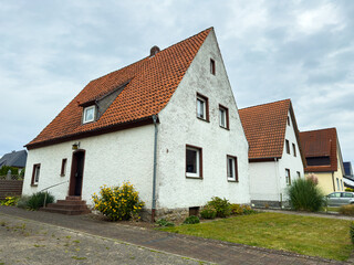 Charming white house with orange roof tiles and lush green garden on a cloudy day in a quiet neighborhood