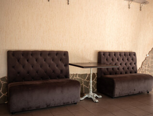 Two brown tufted couches are arranged around a white table with a brown top, creating a cozy...