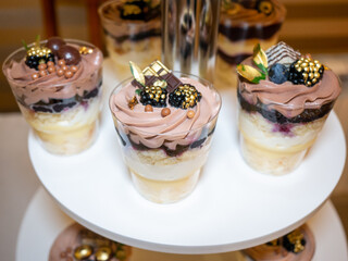 Three glass dessert cups with chocolate and fruit toppings are arranged on a white stand