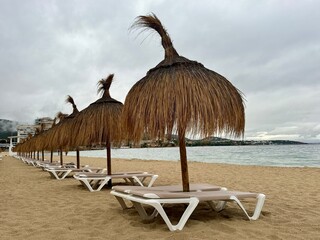 Straw umbrellas and beach sunbeds on sand, Cloudy overcast day at the empty sea beach. Summer vacation is over. off season, no people