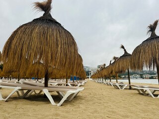 Straw umbrellas and beach sunbeds on sand, Cloudy overcast day at the empty sea beach. Summer vacation is over. off season, no people