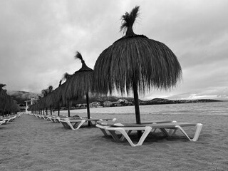 Straw umbrellas and beach sunbeds on sand, Cloudy overcast day at the empty sea beach. Summer vacation is over. off season, no people