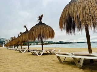 Straw umbrellas and beach sunbeds on sand, Cloudy overcast day at the empty sea beach. Summer vacation is over. off season, no people