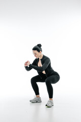 Athletic woman performing squat exercise in black sportswear on white background. Female fitness training, healthy lifestyle and body strength concept.