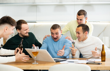 Group of football fans drinking beer and watching football match on a laptop at home