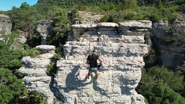 Aerial shot of a man rappelling on Via ferrata Patacons on sunny summer day. Mussara, Tarragona, Spain.