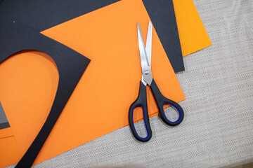 Pair of scissors lying on black and orange craft paper, surrounded by cutouts, representing creative paper crafts or halloween themes