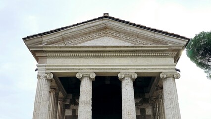 Obraz premium Rome, Italy – 11 January 2025. The Temple of Portunus front view shows its symmetrical Ionic columns, decorated pediment, and sharply defined stone architecture from the Forum Boarium.